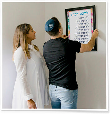 Jewish couple hanging Hebrew Home Blessing on the wall